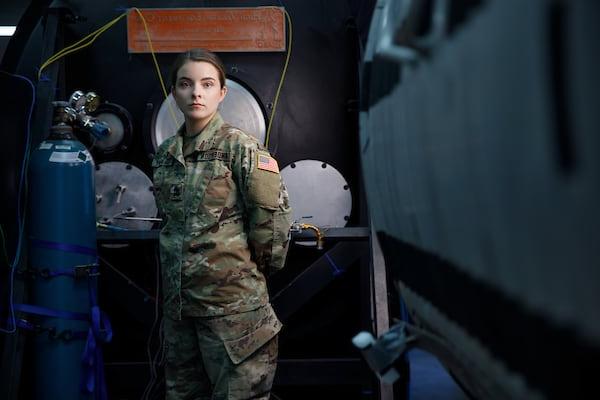 A student in military uniform stands among industrial equipment